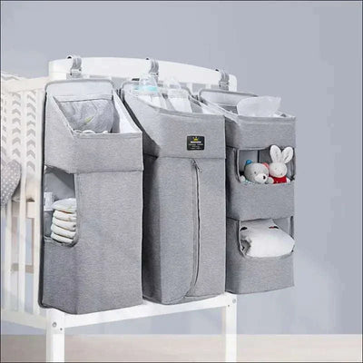 Baby diaper caddy with dividers attached to crib, storing diapers, wipes, and toys.