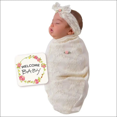 Baby in a lace swaddle and headband with welcome baby card.