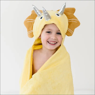Toddler wrapped in a yellow dinosaur hooded towel with silver horns.
