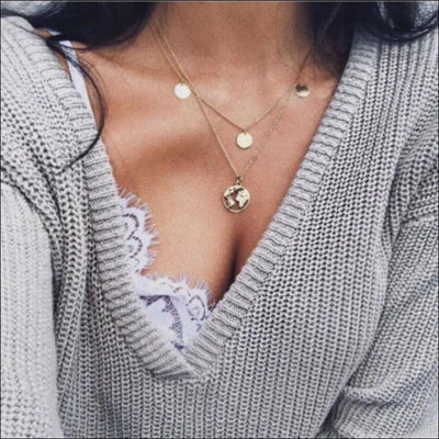Two-layer world map necklace in gold-tone zinc alloy with adjustable length worn on woman in grey sweater and lace top